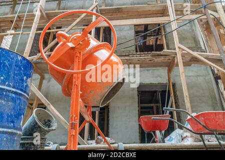 Orangefarbener Betonmischer bereitet Zementmörtel vor. Betonmischer, Fässer vor dem Hintergrund eines im Bau befindlichen Hauses aus nächster Nähe Stockfoto