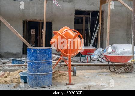 Orangefarbener Betonmischer bereitet Zementmörtel vor. Betonmischer, Fässer vor dem Hintergrund eines im Bau befindlichen Hauses aus nächster Nähe Stockfoto