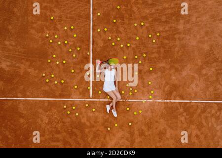 Portrait einer lächelnden Frau, die sich nach hartem Tennistraining im Freien auf dem Tennisplatz mit vielen Bällen und Schlägern entspannt. Dolly-Schuss. Draufsicht Stockfoto