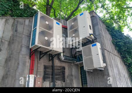 Drei große Klimaanlagen an einer Betonwand im Straße zwischen den grünen Stockfoto