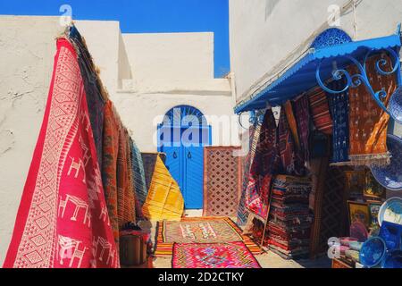 Shop Verkauf von Teppichen, Souvenirs und Stoffen im Basar in der Medina, Sidi Bou Said, Tunesien. An blauen Wänden hängen traditionelle tunesische Teppiche Stockfoto