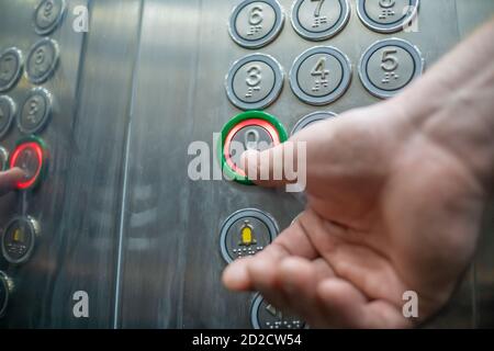 Der Daumen drückt die Taste in der Nahaufnahme des Elevator Zero Floor. Die Aufzugsknöpfe sind in Braille-Schrift signiert. Das Konzept der Inklusion. Stockfoto