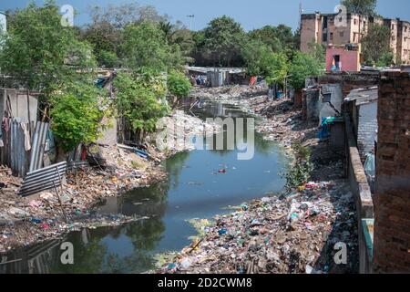 Ein Fluss gefüllt mit Plastikmüll Entsorgung umgeben von Gebäuden und Bäumen in den Slums von Chennai, Tamil Nadu, Indien Stockfoto