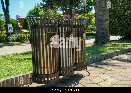 Moderne Metallbehälter für die getrennte Abfallsammlung im Park an einem sonnigen Tag aus nächster Nähe. Übersetzung: 'Plastik, Glas, Papier.' Stockfoto