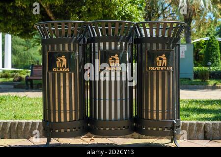 Moderne Metallbehälter für die getrennte Abfallsammlung im Park an einem sonnigen Tag aus nächster Nähe. Übersetzung: 'Plastik, Glas, Papier.' Stockfoto