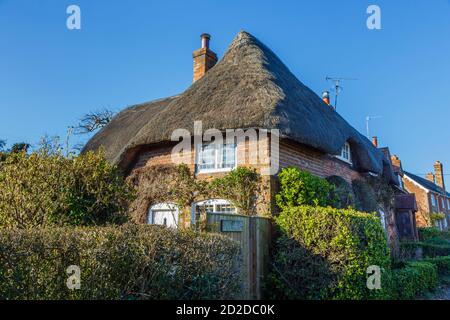 Ein traditionelles rotes Backsteinhaus mit Reetgedeckten, Cobbler's Cottage, gesehen an einem sonnigen Tag im Dorf von Great Bedwyn, Wiltshire, Südengland Stockfoto