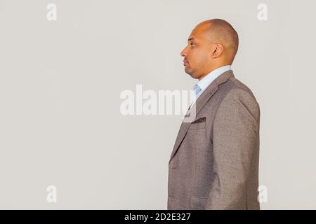 Hübscher junger afroamerikanischer Geschäftsmann in einer Jacke, im Profil stehend, zur Seite schauend, posiert für ein Foto auf einem grauen Hintergrund. Stockfoto