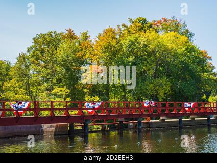 Fußgängerbrücke über einen Damm auf einem Teich mit patriotischen roten, weißen und blauen Fahnen weht in den Wind Stockfoto