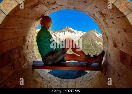 Wanderfrau, die sich nach dem Trekking in den Berner Alpen, Kanton Wallis, Europa, in der Holzbank entspannt. Frau schaut Aletsch Gletscher aus Stockfoto