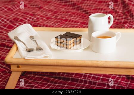 Tasse Kaffee mit Milch und Schokoladenkuchen. Süßes köstliches Frühstück auf einem Tisch mit Betttablett Stockfoto