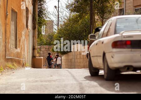 Hama, Syrien 04/02/2010: Trotz Autos, die die Straße benutzen, spielen und fahren Kinder auf einer engen Straße in einem alten und armen Viertel von Hama wh Stockfoto