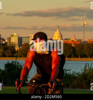 Washington DC, USA 10/02/2020: Ein hispanischer Radfahrer mit Gesichtsmaske wegen COVID-19 fährt bei Sonnenuntergang in einem Stadtpark am Gravelly Point in DC mit Stockfoto