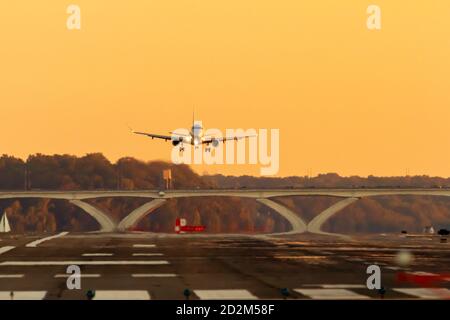 Eine Passagierfluggesellschaft steigt langsam auf eine Landebahn bei Sonnenuntergang. Die Lichter des Flugzeugs sind an und die Räder sind unten. Es gibt landschaftlich schönen Sonnenuntergang Himmel Stockfoto