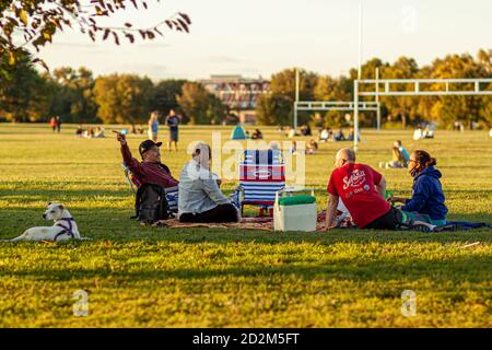 Arlington, VA, USA 10/02/2020: Eine multirassische Gruppe junger Menschen sitzen auf zusammenklappbaren Stühlen oder Laken auf dem Grasfeld des Gravelly Point Parks. Th Stockfoto