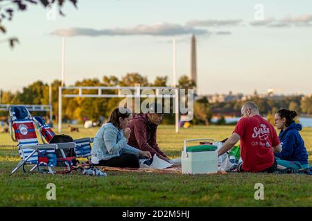 Arlington, VA, USA 10/02/2020: Eine multirassische Gruppe junger Menschen sitzen auf zusammenklappbaren Stühlen oder Laken auf dem Grasfeld des Gravelly Point Parks. Th Stockfoto