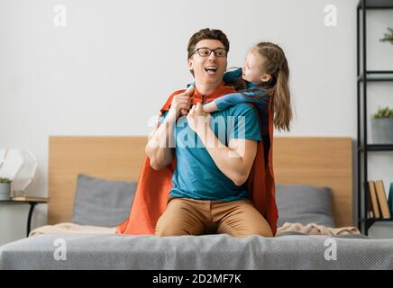 Vater und sein Kind spielen zusammen. Mädchen und Vater im Superhelden Kostüm. Papa und Kind haben Spaß, lächeln und umarmen. Familienurlaub und Zweisamkeit Stockfoto