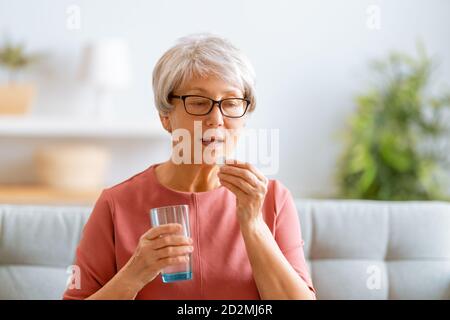 Ältere Frau hält Pille und Glas frisches Wasser, Einnahme von Medikamenten gegen Kopfschmerzen, Magenschmerzen oder Einnahme von Vitaminen, Sedierung Medikamente. Stockfoto