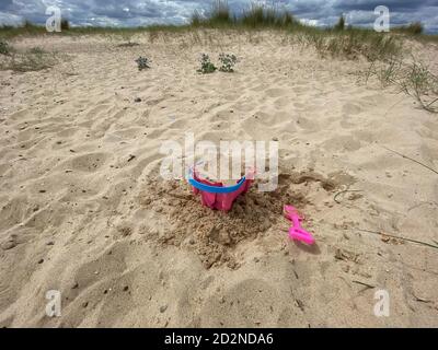 Pink Basket und Spaten auf Great Yarmouth Strand in einem kalten Sommertag, traditionelle englische Küste, Himmel mit Wolken keine Menschen, große Strecke des Sandes, Großbritannien sein Stockfoto