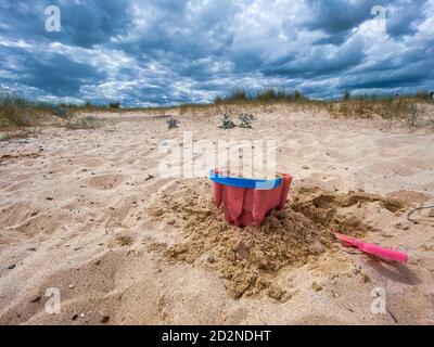 Pink Basket und Spaten auf Great Yarmouth Strand in einem kalten Sommertag, traditionelle englische Küste, Himmel mit Wolken keine Menschen, große Strecke des Sandes, Großbritannien sein Stockfoto