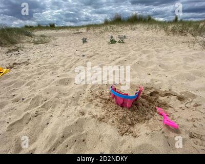 Pink Basket und Spaten auf Great Yarmouth Strand in einem kalten Sommertag, traditionelle englische Küste, Himmel mit Wolken keine Menschen, große Strecke des Sandes, Großbritannien sein Stockfoto