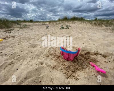 Pink Basket und Spaten auf Great Yarmouth Strand in einem kalten Sommertag, traditionelle englische Küste, Himmel mit Wolken keine Menschen, große Strecke des Sandes, Großbritannien sein Stockfoto