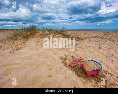 Pink Basket und Spaten auf Great Yarmouth Strand in einem kalten Sommertag, traditionelle englische Küste, Himmel mit Wolken keine Menschen, große Strecke des Sandes, Großbritannien sein Stockfoto