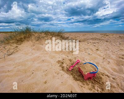 Pink Basket und Spaten auf Great Yarmouth Strand in einem kalten Sommertag, traditionelle englische Küste, Himmel mit Wolken keine Menschen, große Strecke des Sandes, Großbritannien sein Stockfoto