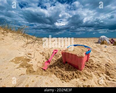 Pink Basket und Spaten auf Great Yarmouth Strand in einem kalten Sommertag, traditionelle englische Küste, Himmel mit Wolken keine Menschen, große Strecke des Sandes, Großbritannien sein Stockfoto