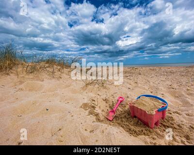 Pink Basket und Spaten auf Great Yarmouth Strand in einem kalten Sommertag, traditionelle englische Küste, Himmel mit Wolken keine Menschen, große Strecke des Sandes, Großbritannien sein Stockfoto