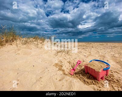 Pink Basket und Spaten auf Great Yarmouth Strand in einem kalten Sommertag, traditionelle englische Küste, Himmel mit Wolken keine Menschen, große Strecke des Sandes, Großbritannien sein Stockfoto