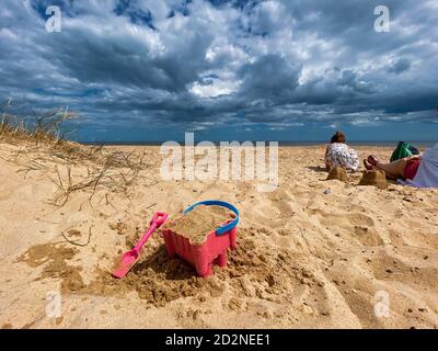 Pink Basket und Spaten auf Great Yarmouth Strand in einem kalten Sommertag, traditionelle englische Küste, Himmel mit Wolken keine Menschen, große Strecke des Sandes, Großbritannien sein Stockfoto