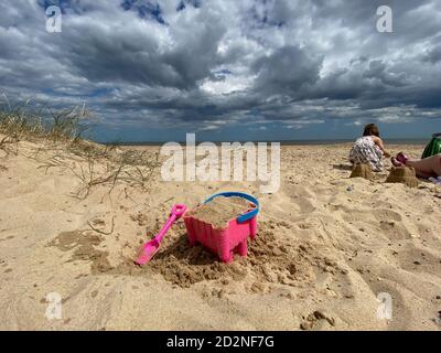 Pink Basket und Spaten auf Great Yarmouth Strand in einem kalten Sommertag, traditionelle englische Küste, Himmel mit Wolken keine Menschen, große Strecke des Sandes, Großbritannien sein Stockfoto