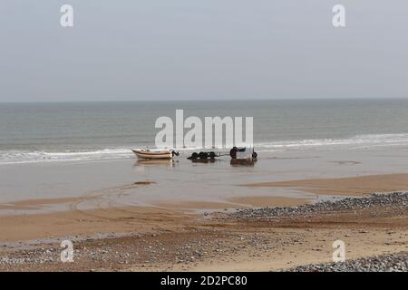 Fischerboote auf dem Sandstrand von Cromer an einem sonnigen Wintertag, Muschel Meer mit sanften Wellen krachend auf den Strand Stockfoto