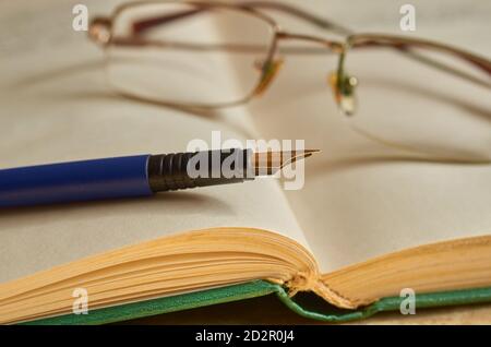 Brille und blauer Füllfederhalter liegen auf einem offenen Buch. Nahaufnahme Stockfoto