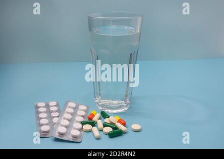 Vitamine und Pillen auf blauem Hintergrund. Glas Wasser für die Einnahme von Medikamenten. Seitenansicht, Nahaufnahme, selektiver Fokus. Stockfoto