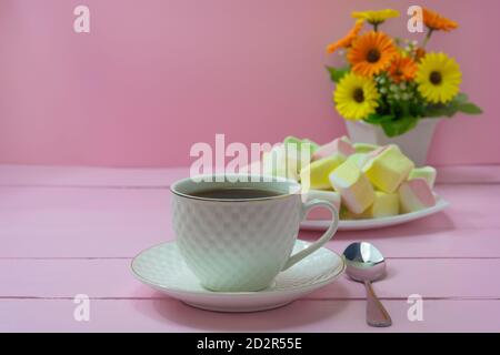 Nahaufnahme Kaffeetasse auf rosa Holzhintergrund. Süße Marshmallows und Blumenstrauß. Roma Frühstückskonzept, Zärtlichkeit, Guten Morgen. Stockfoto