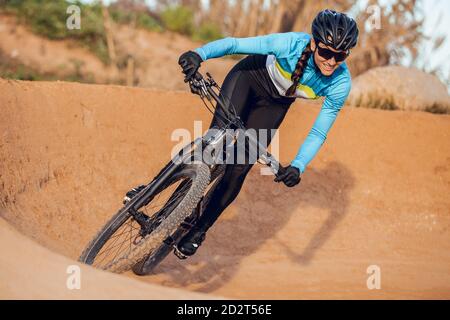 Sportlerin in schwarzem Helm und blauer Sportbekleidung mit Brille auf dem Mountainbike auf der Trainingsstrecke Stockfoto