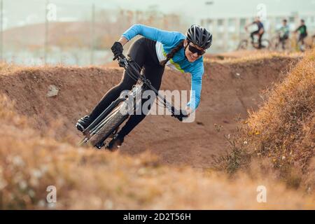 Sportlerin in schwarzem Helm und blauer Sportbekleidung mit Brille auf dem Mountainbike auf der Trainingsstrecke Stockfoto