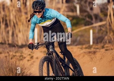 Sportlerin in schwarzem Helm und blauer Sportbekleidung mit Brille auf dem Mountainbike auf der Trainingsstrecke Stockfoto