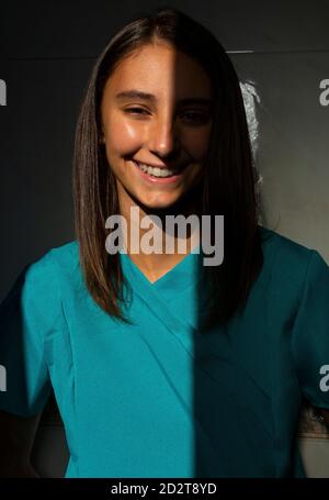 Fröhliche Ärztin trägt blauen medizinischen Kleid im Krankenhaus stehen Und Blick auf die Kamera Stockfoto