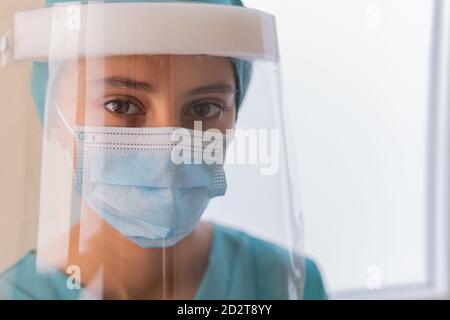 Ernsthafte weibliche Sanitäter in schützenden Gesichtsschild und Maske suchen Während der Arbeit im Krankenhaus während einer Coronavirus-Pandemie vor der Kamera Stockfoto