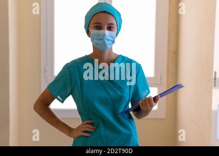 Konzentrierte junge Krankenschwester in blauer Uniform und Maske mit Klemmbrett Während der Arbeit im Krankenhaus Stockfoto