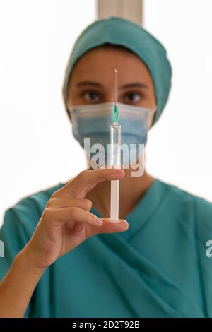 Professionelle medizinische Mitarbeiterin in Schutzmaske hält Spritze mit Medizin während der Vorbereitung für die Injektion im Krankenhaus Stockfoto