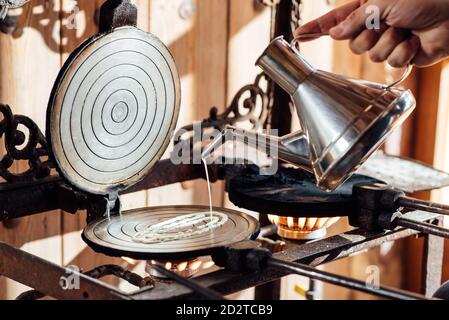 Crop anonyme Person Gießen flüssigen Teig aus Metall Kessel auf Waffeleisen auf Gasherd platziert, während die Zubereitung typisch katalanisch Neula Kekse in der Küche Stockfoto