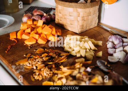 Frisch gehackter Kürbis und Kartoffel mit Zwiebel auf Holz angeordnet Brett mit Zutaten während der Zubereitung der Sahnesuppe zu Hause Küche Stockfoto