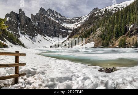 Majestätische Landschaft des gefrorenen Moraine Lake umgeben von grünen Nadelbäumen Wald und raue felsige Berge bedeckt mit Schnee in bewölkt Tag im Banff National Park in Kanada Stockfoto