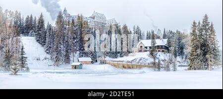 Panoramalandschaft mit Dorfgebäuden umgeben von Nadelbäumen Hügeliges Gelände im Winter mit Schnee bedeckt Stockfoto