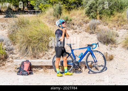 Ganzkörper-Seitenansicht des sportlichen männlichen Radfahrers in der Aktivbekleidung Mit Rucksack in der Nähe des Fahrrads und Einstellhelm während der Vorbereitung stehen Für das Reiten Workout im Sommer Natur Stockfoto