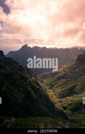 Malerische Aussicht auf Serpentin Asphaltstraße durch felsige Berge Bedeckt mit grünen Pflanzen am Morgen in Teneriffa Stockfoto