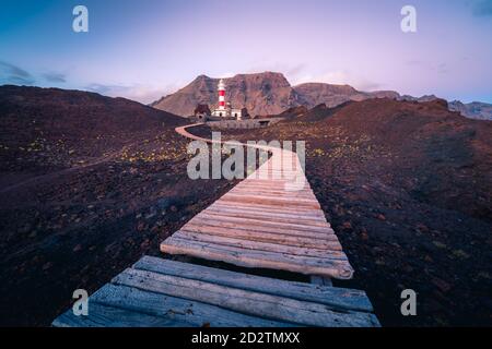 Kurvenreicher Pfad, der zum Leuchtturm führt, der sich auf einem Hügel in der Nähe des Meeres befindet Auf dem Hintergrund der Berge am Morgen in Teneriffa Stockfoto